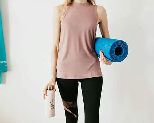 A woman holding a yoga mat and water bottle.